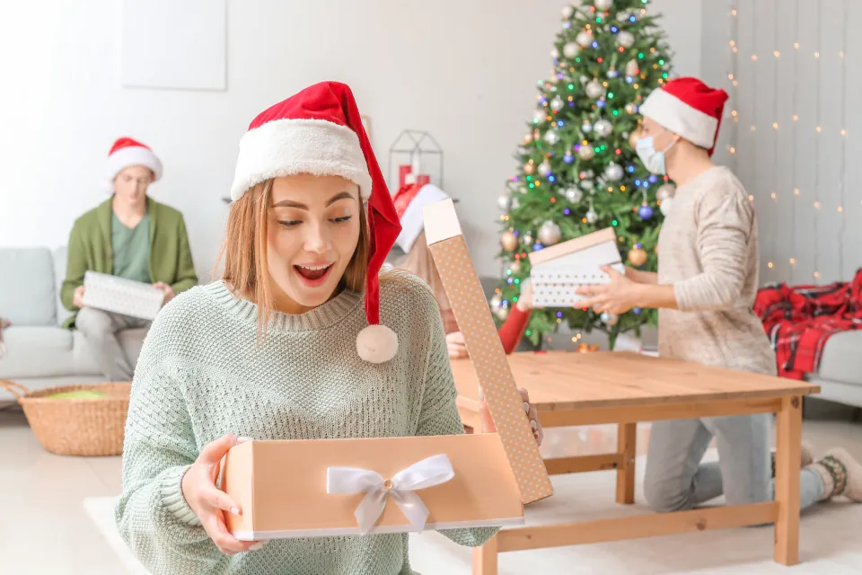 Une femme ouvre un cadeau, surprise, près du sapin